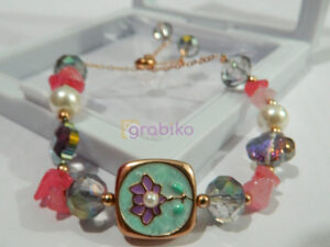 A handcrafted multicolored beaded bracelet featuring a floral charm centerpiece with pearl and crystal accents, displayed in a jewelry box.