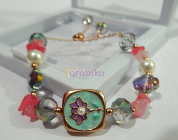 A handcrafted multicolored beaded bracelet featuring a floral charm centerpiece with pearl and crystal accents, displayed in a jewelry box.