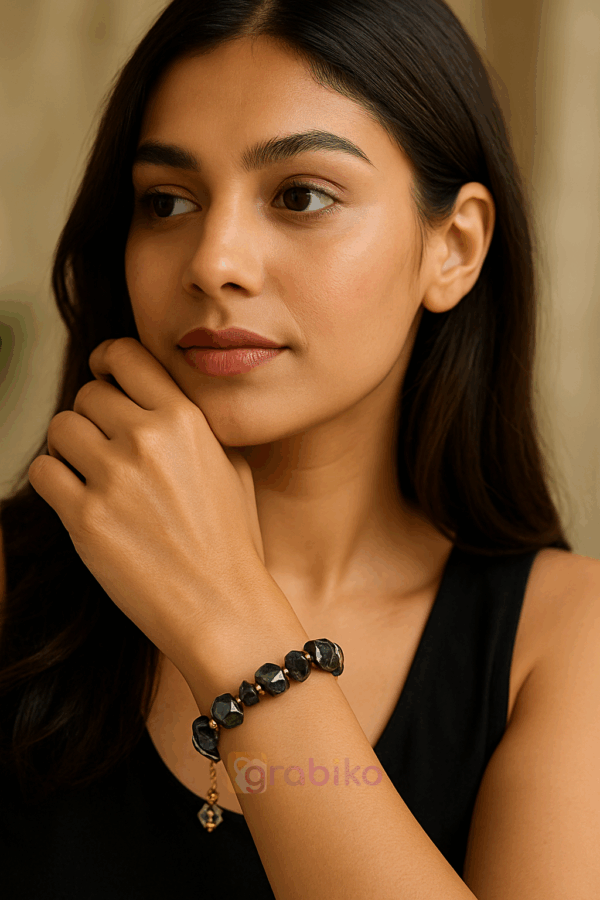 Black crystal beaded bracelet with adjustable golden chain, featuring faceted glass and cube-shaped beads, displayed in a white jewelry box.