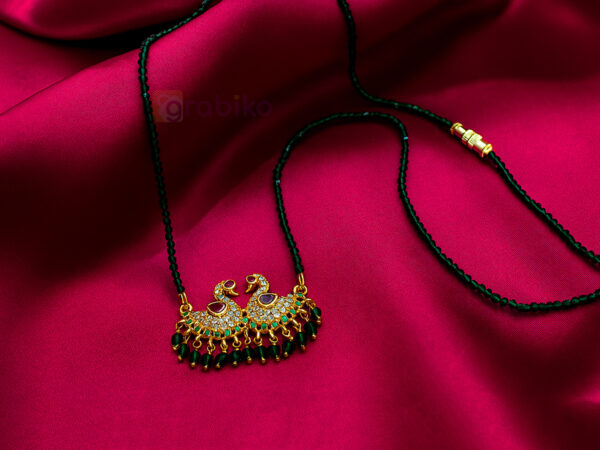 Elegant double peacock mangalsutra with CZ stones and green beads on pink fabric background